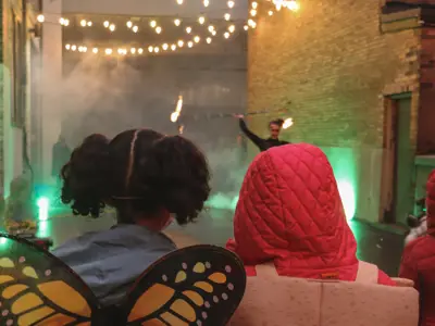 view of kids' backs as they watch a fire performer in an alley